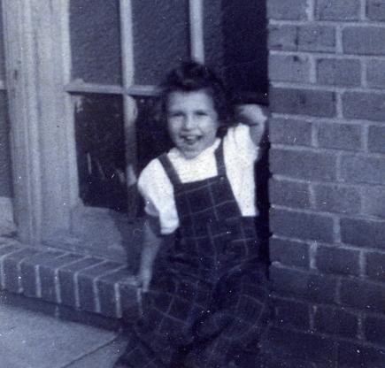 Lois as a small girl in overalls, laughing on a brick doorstep
