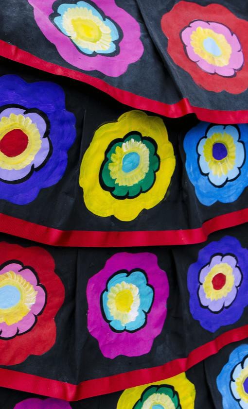 Rows of bright hand-painted flowers, each a different color, on black cloth trimmed with red ribbon
