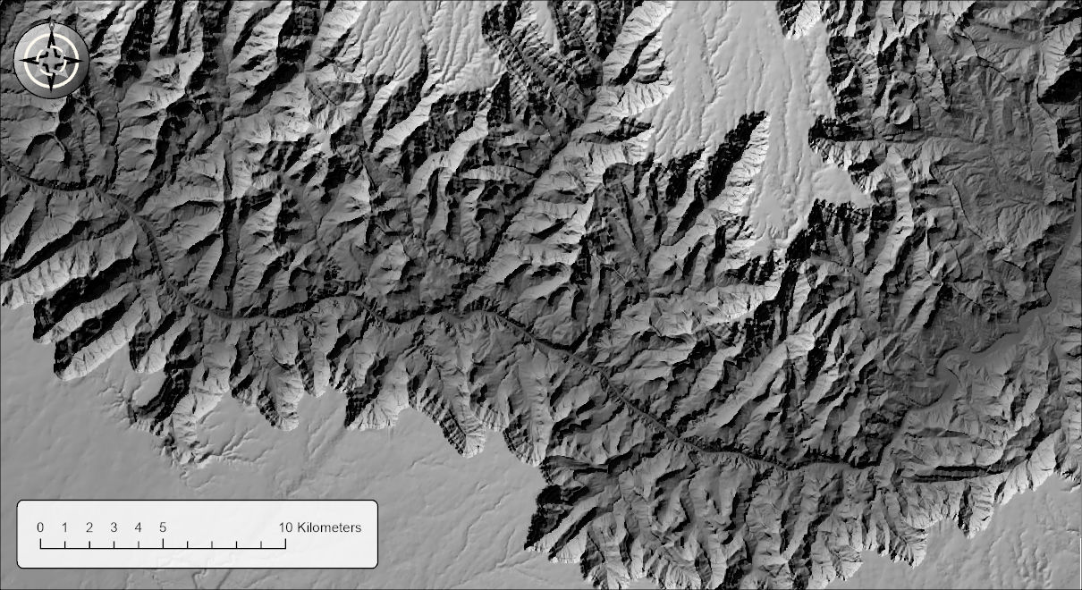 A gray hillshade of the Grand Canyon lit from the northwest: the inner gorge and the low side canyons are darkened, the high plateaus are pale, and the cast shadows behind the canyon walls are dark but still show the texture of the ground inside them
