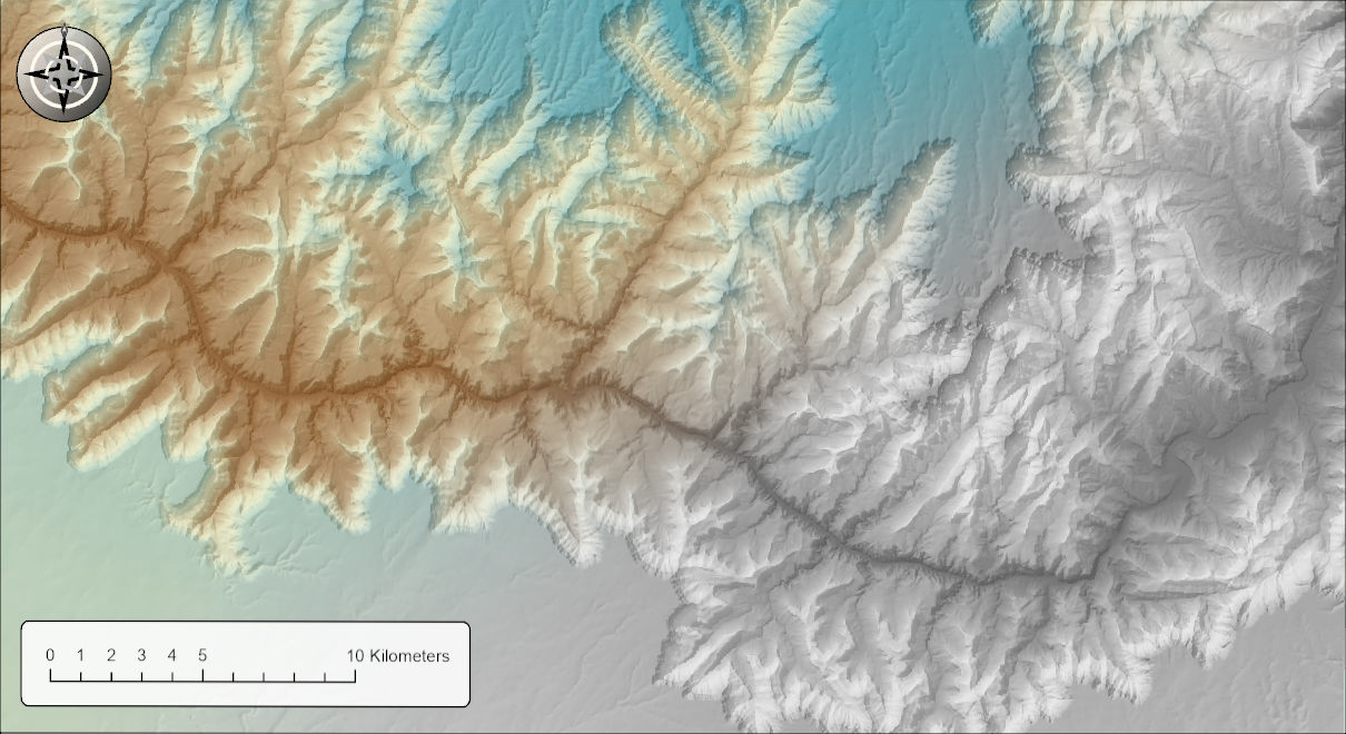 A hillshade of the Grand Canyon under a partially transparent DEM drawn in a color ramp. In the upper left the picture is in color, with a brown inner canyon grading through pale yellow to blue-green on the high plateaus; the color fades toward the lower right, where the same picture is entirely gray