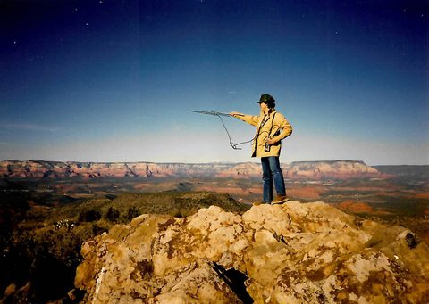 Jeff Jenness standing on a rock outcrop holding a hand-held radio-telemetry antenna, with red-rock cliffs and a wide valley behind
