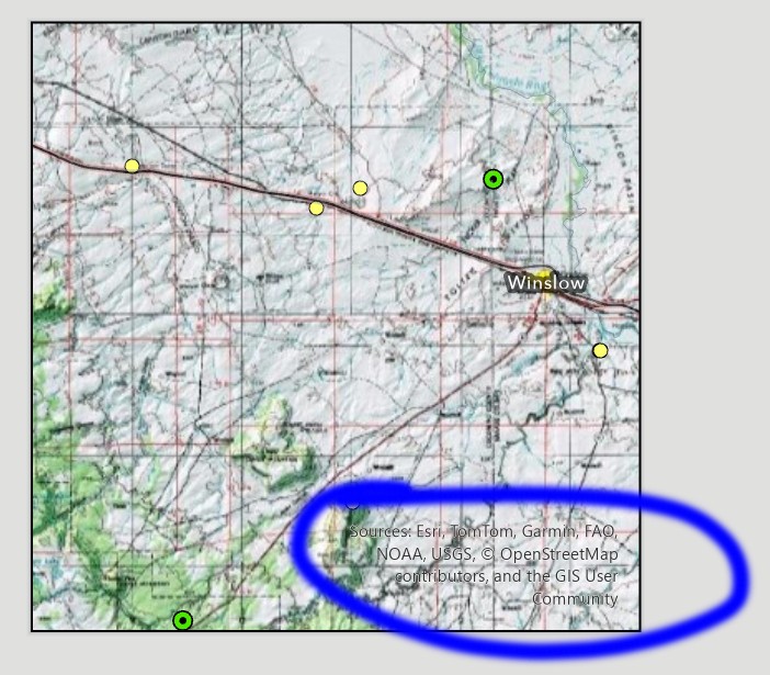A layout's map frame showing a topographic map around Winslow, Arizona, with green and yellow point symbols. In the lower right corner of the map frame, printed over the map, is the text: Sources: Esri, TomTom, Garmin, FAO, NOAA, USGS, copyright OpenStreetMap contributors, and the GIS User Community. The text is circled in blue